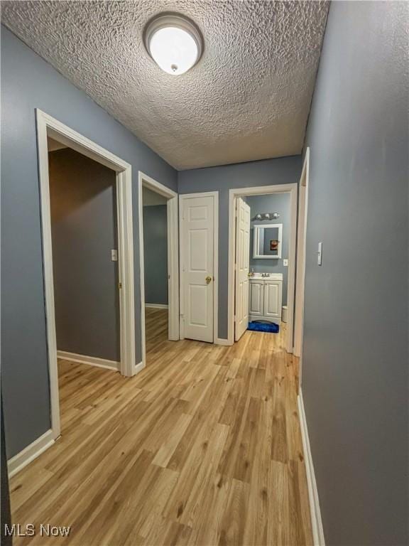 corridor with a textured ceiling and light wood-type flooring