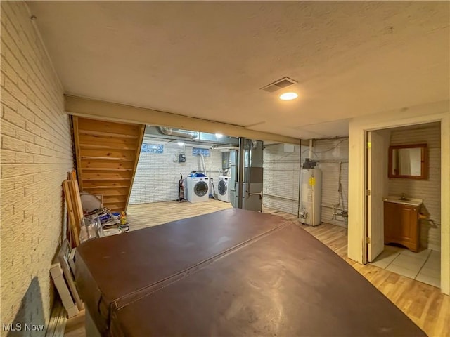 basement featuring heating unit, independent washer and dryer, water heater, and light wood-type flooring