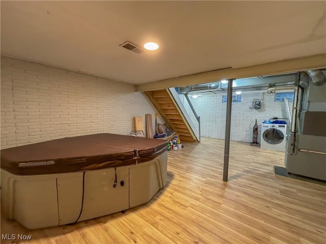 basement with washer and dryer, brick wall, light hardwood / wood-style flooring, and heating unit