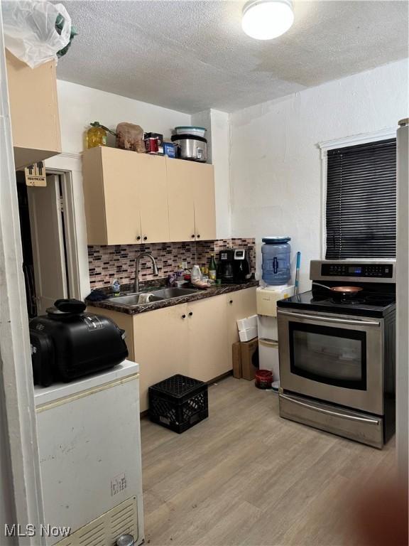 kitchen with sink, light hardwood / wood-style flooring, stainless steel range with electric stovetop, backsplash, and cream cabinets