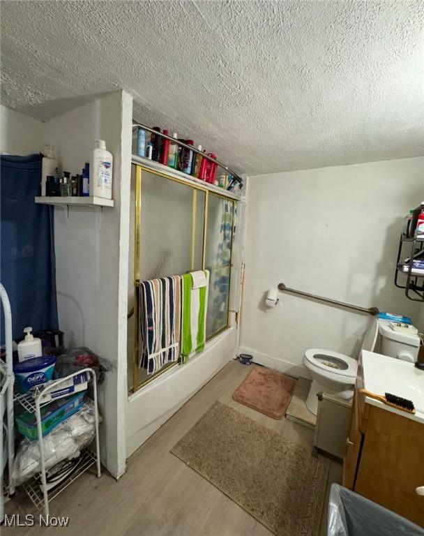 bathroom featuring toilet, a shower with shower door, wood-type flooring, a textured ceiling, and vanity