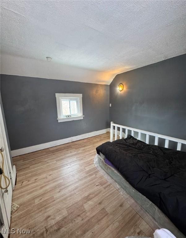 bedroom with lofted ceiling, light hardwood / wood-style floors, and a textured ceiling