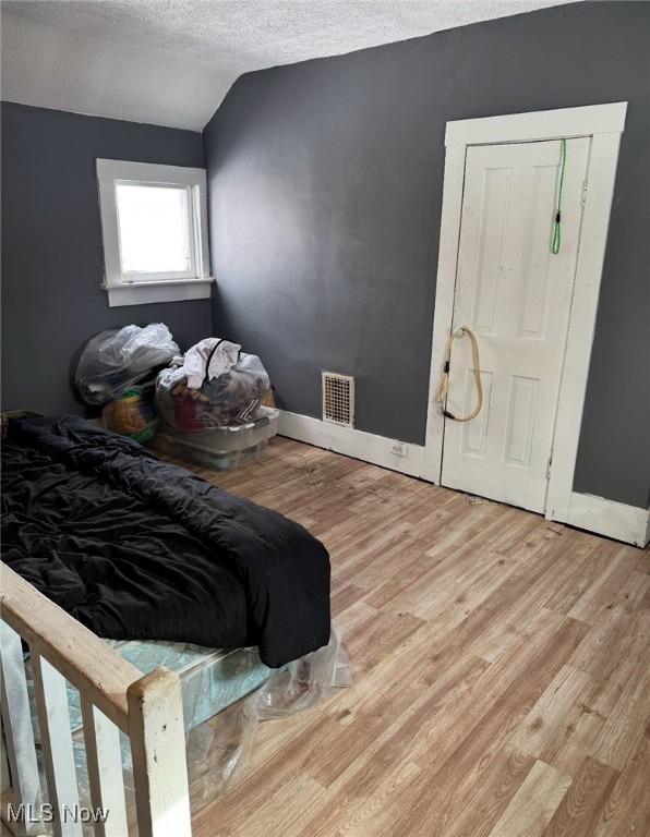 bedroom featuring vaulted ceiling, a textured ceiling, and light hardwood / wood-style flooring