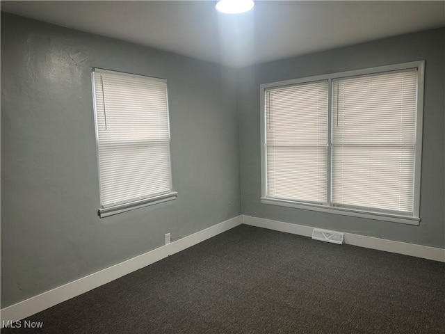 empty room featuring dark carpet and a wealth of natural light