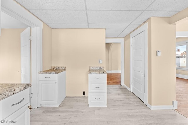 interior space with a drop ceiling, white cabinetry, and light hardwood / wood-style floors