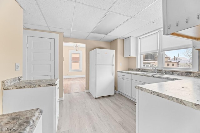 kitchen with white refrigerator, white cabinetry, sink, and a drop ceiling