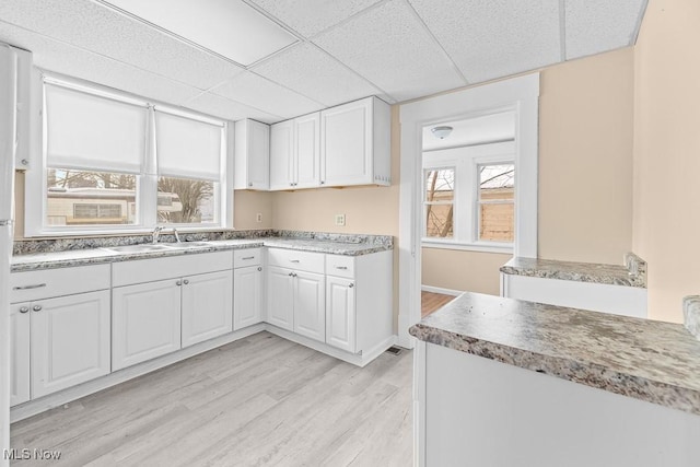 kitchen with sink, a drop ceiling, white cabinets, and light hardwood / wood-style floors