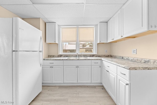 kitchen with a paneled ceiling, sink, white cabinets, white fridge, and light hardwood / wood-style floors