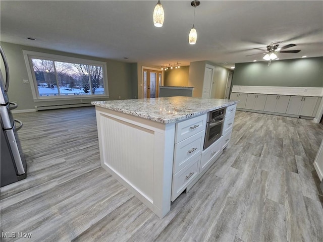 kitchen featuring decorative light fixtures, white cabinets, a center island, stainless steel oven, and light stone counters