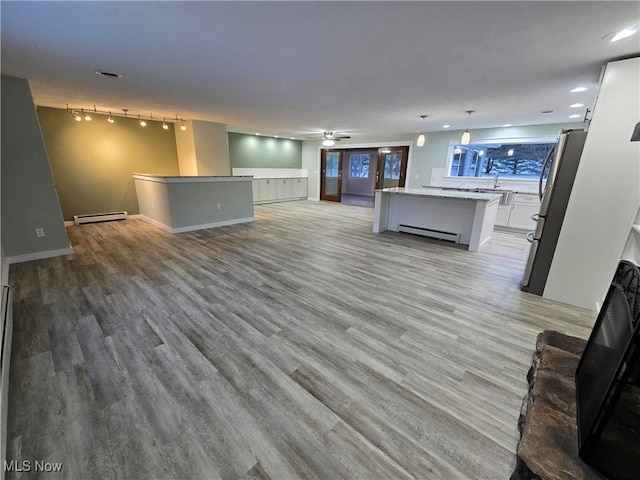 unfurnished living room featuring sink, light hardwood / wood-style flooring, track lighting, and baseboard heating