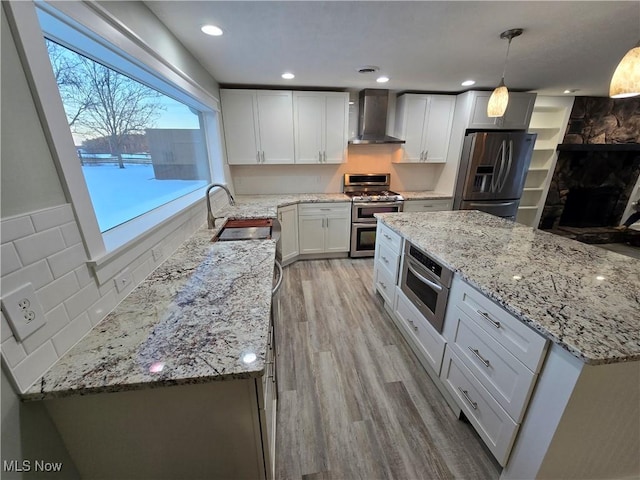 kitchen with wall chimney exhaust hood, sink, white cabinetry, pendant lighting, and stainless steel appliances