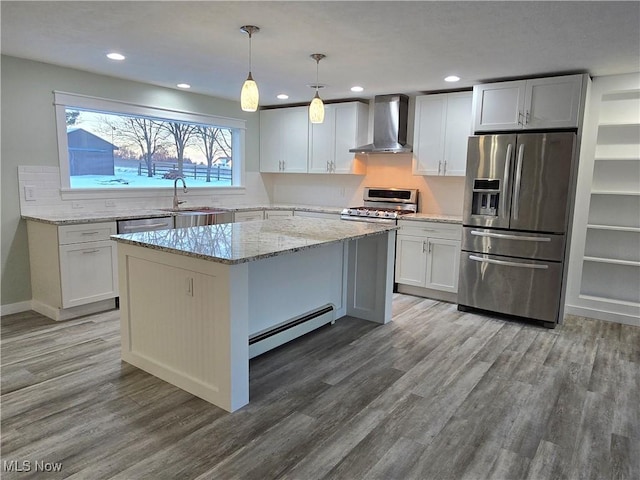 kitchen with wall chimney range hood, appliances with stainless steel finishes, a kitchen island, decorative light fixtures, and a baseboard radiator