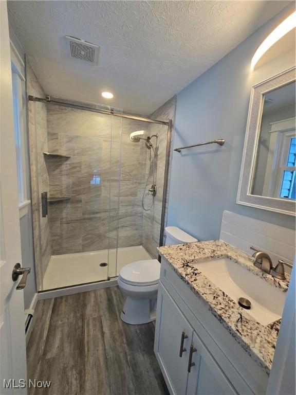 bathroom featuring walk in shower, toilet, a textured ceiling, vanity, and hardwood / wood-style flooring