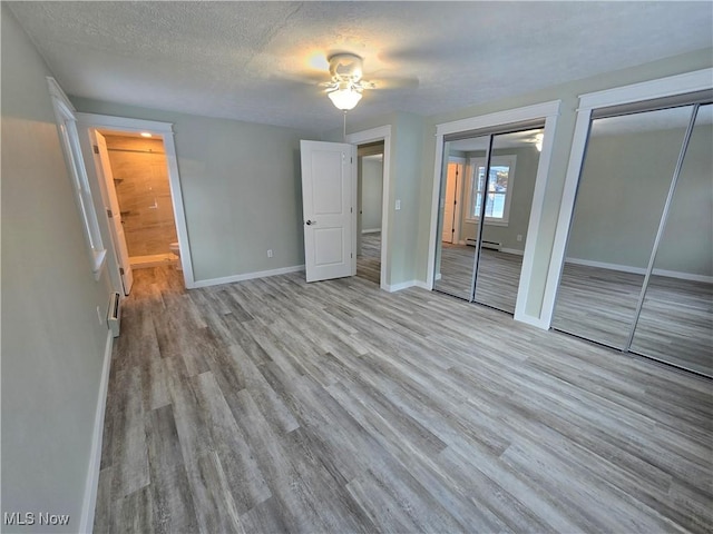 unfurnished bedroom with a textured ceiling, a baseboard radiator, two closets, ceiling fan, and light hardwood / wood-style floors