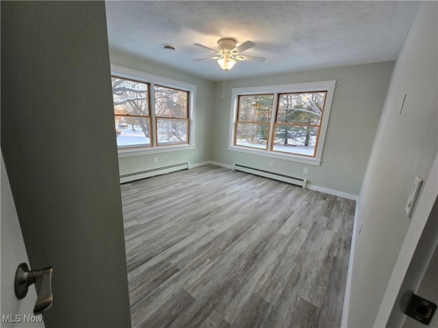 spare room featuring ceiling fan, a textured ceiling, baseboard heating, and light hardwood / wood-style flooring