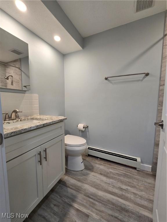 bathroom featuring toilet, tasteful backsplash, wood-type flooring, a baseboard radiator, and vanity