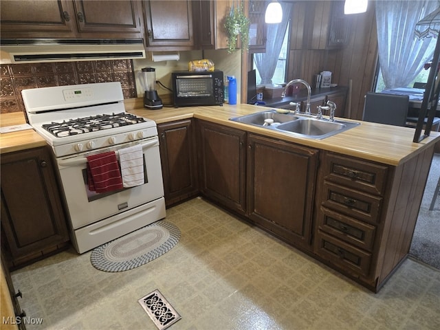 kitchen featuring a wealth of natural light, sink, white range with gas stovetop, and dark brown cabinetry