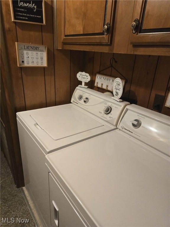 clothes washing area with cabinets, wooden walls, and independent washer and dryer