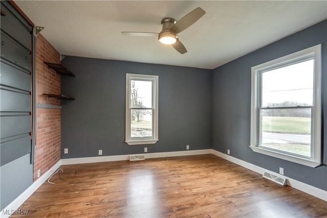 unfurnished room with a large fireplace, ceiling fan, and light wood-type flooring