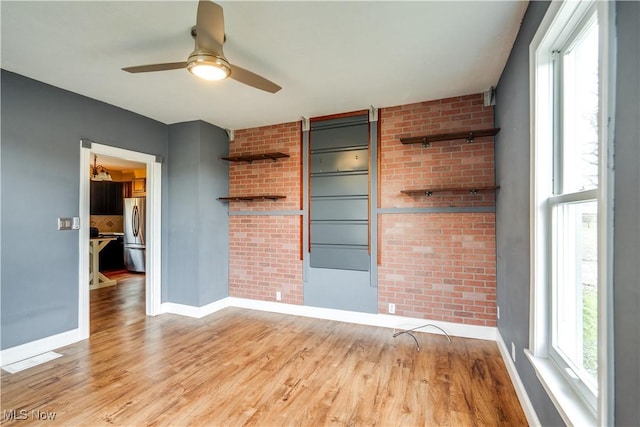 spare room featuring brick wall, light wood-type flooring, and ceiling fan