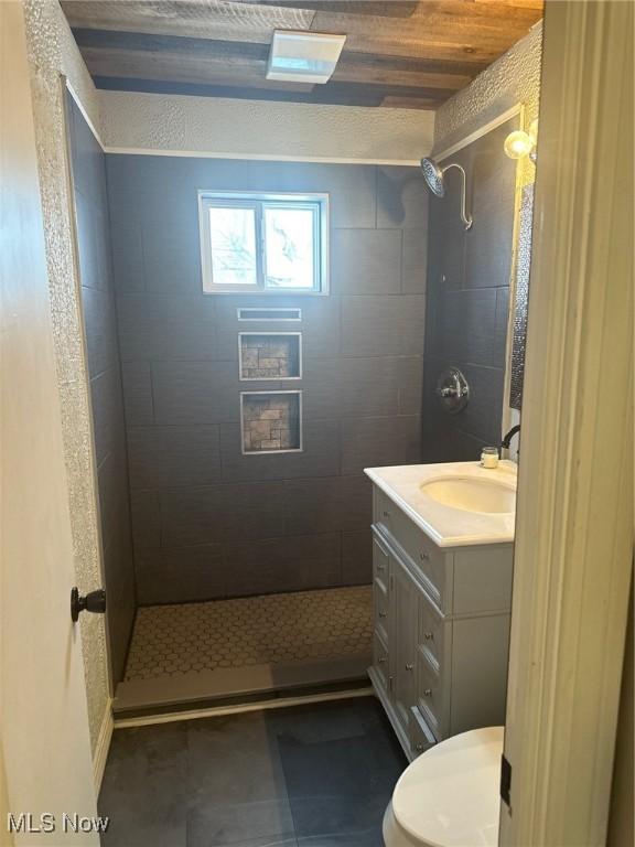 bathroom featuring wood ceiling, tiled shower, vanity, and toilet