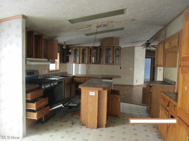 kitchen featuring a breakfast bar, stainless steel gas stove, a center island, a textured ceiling, and ceiling fan