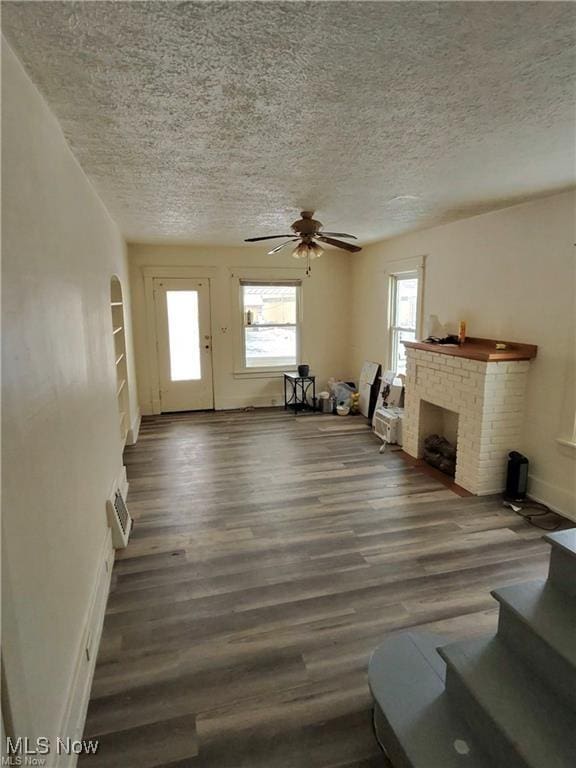 unfurnished living room featuring ceiling fan, a brick fireplace, a textured ceiling, and dark hardwood / wood-style flooring