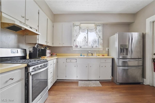 kitchen featuring sink, wood-type flooring, a textured ceiling, appliances with stainless steel finishes, and white cabinets