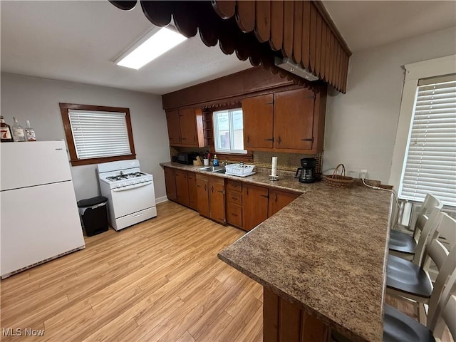 kitchen featuring white appliances, plenty of natural light, kitchen peninsula, and light hardwood / wood-style flooring