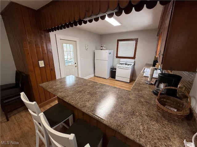 kitchen featuring a breakfast bar area, kitchen peninsula, white appliances, and light hardwood / wood-style flooring