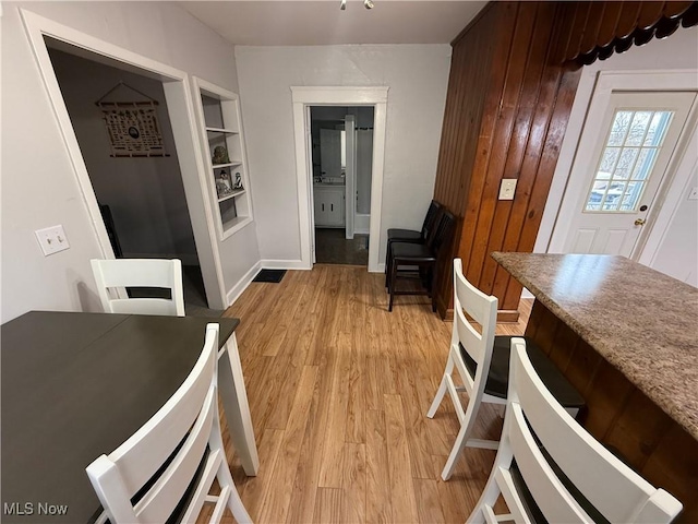 dining area with wooden walls, built in features, and light wood-type flooring