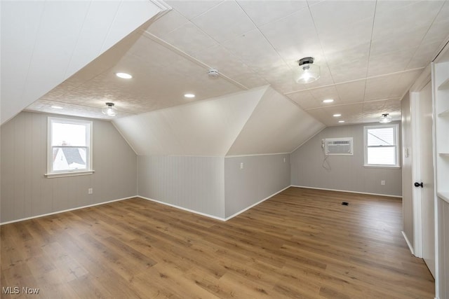 additional living space featuring a healthy amount of sunlight, vaulted ceiling, wood-type flooring, and an AC wall unit