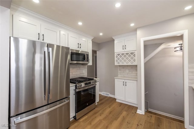 kitchen with tasteful backsplash, light wood-type flooring, white cabinets, and appliances with stainless steel finishes