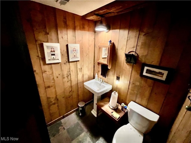 bathroom with toilet, sink, and wood walls