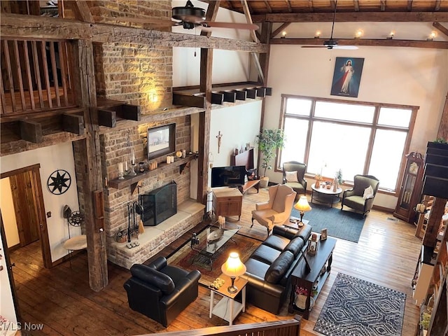 living room with ceiling fan, hardwood / wood-style floors, beam ceiling, high vaulted ceiling, and a stone fireplace