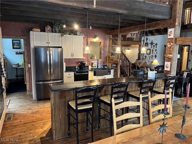 kitchen featuring stainless steel fridge, black dishwasher, white cabinets, a kitchen bar, and decorative light fixtures