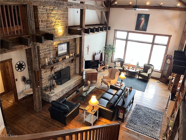 living room featuring a stone fireplace, a towering ceiling, ceiling fan, and hardwood / wood-style flooring