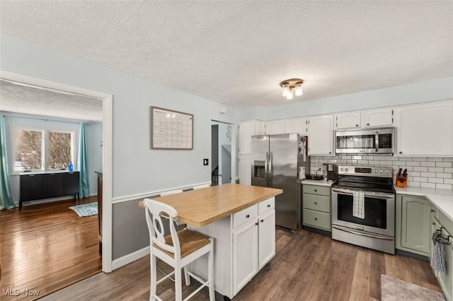 kitchen with dark wood-type flooring, appliances with stainless steel finishes, white cabinets, a kitchen bar, and decorative backsplash