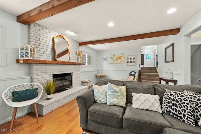 living room with a brick fireplace, beam ceiling, light hardwood / wood-style floors, and a textured ceiling