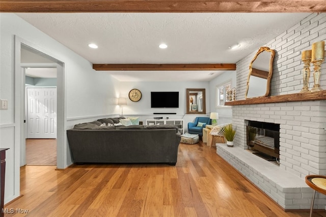 living room featuring a brick fireplace, light wood-type flooring, and a textured ceiling