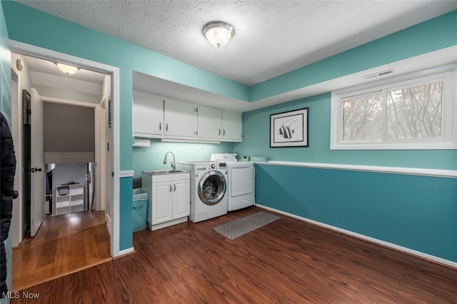 laundry room featuring sink, dark hardwood / wood-style flooring, cabinets, washer and clothes dryer, and a textured ceiling