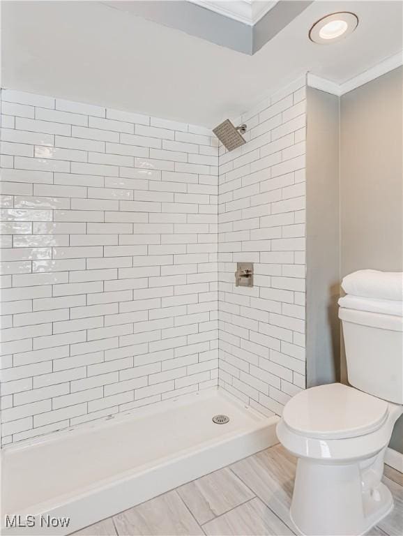 bathroom with ornamental molding, toilet, and a tile shower