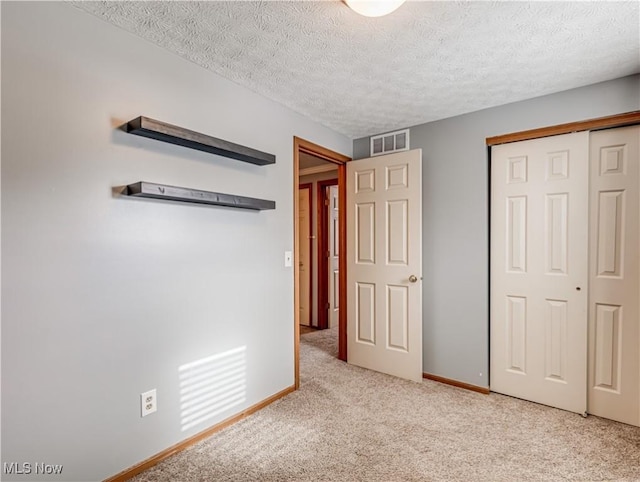 unfurnished bedroom with light colored carpet, a closet, and a textured ceiling