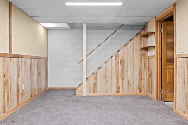 basement with light carpet, a paneled ceiling, and wood walls