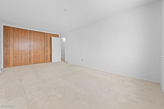 unfurnished bedroom with carpet floors, wooden walls, and a closet