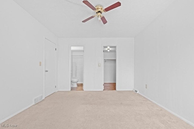 unfurnished bedroom with ensuite bathroom, a spacious closet, light colored carpet, a closet, and ceiling fan