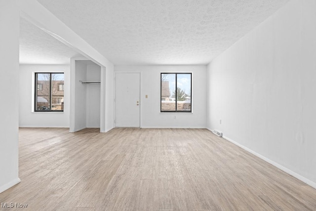 unfurnished room featuring a healthy amount of sunlight, light hardwood / wood-style floors, and a textured ceiling