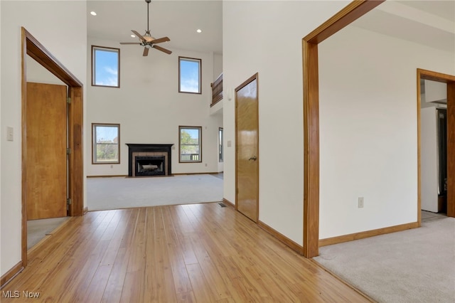 unfurnished living room with ceiling fan, light hardwood / wood-style flooring, and a high ceiling