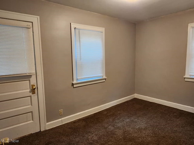 spare room featuring dark carpet and baseboards