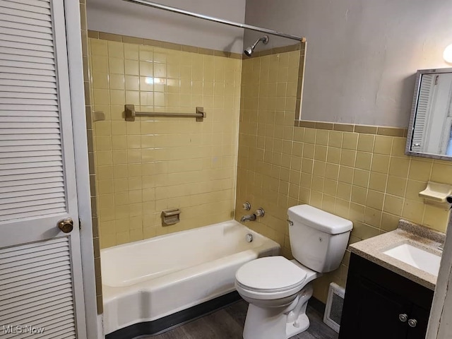 full bathroom with hardwood / wood-style floors, tile walls, tiled shower / bath combo, vanity, and toilet